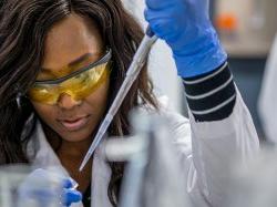 在科学与数学学院，一名学生穿着实验服，戴着护目镜向小容器中注射液体